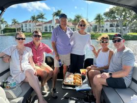 A cheerful group enjoys a delightful day on a pontoon boat, sharing food and laughter against a picturesque waterfront backdrop.