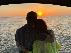 A couple embraces while watching a stunning sunset over the water, creating a perfect romantic moment on their boating adventure.