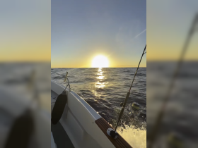 A serene view of a fishing boat at sunset, with the sun reflecting on the water's surface — perfect for capturing the tranquility of a day on the sea.