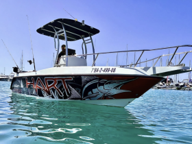 A striking speedboat named 'HART' is docked in clear turquoise waters, showcasing its vibrant design and fishing gear, perfect for a day out on the water.