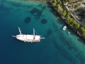 Aerial view of a beautiful yacht anchored in crystal-clear waters, showcasing the serene coastal landscape and vibrant marine environment.