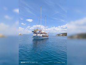 A beautiful sailboat anchored in calm waters, showcasing its elegant design against a backdrop of clear blue skies and distant hills.