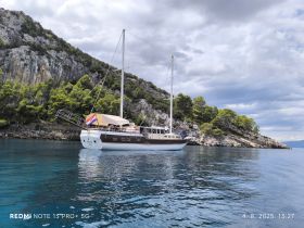 A beautiful sailboat anchored near a rocky coastline, showcasing the serene waters and lush greenery — perfect for exploring coastal destinations.