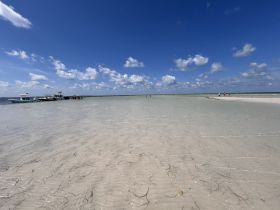 A vibrant scene at a sandbar with boats anchored nearby and groups of people enjoying the beach — perfect for a fun day on the water.