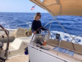 A woman navigates a sailboat on the open ocean, showcasing the thrill of sailing and the beauty of the sea.