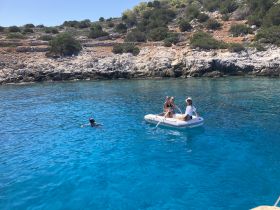 A group enjoys a sunny day on the water, with one person snorkeling and others relaxing in a small boat — a perfect scene for summer adventures and aquatic fun.