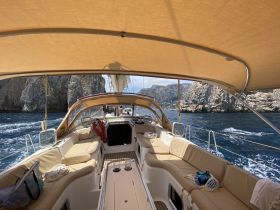 A cozy interior view of a yacht's cabin, featuring comfortable seating and a serene backdrop of rocky cliffs — perfect for relaxing while cruising.