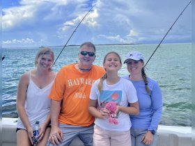 A joyful family poses together on a fishing trip, showcasing smiles and camaraderie against a beautiful ocean backdrop.