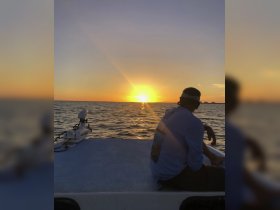 A serene sunset view from a boat, with a person enjoying the tranquil moment — perfect for capturing the beauty of evening cruises.
