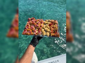 A delicious spread of charcuterie and snacks is presented on a platter, perfect for enjoying while on a boat trip in clear turquoise waters.
