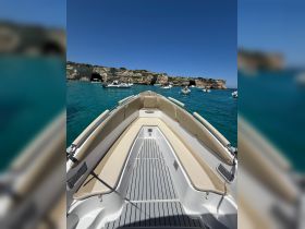 A clear view of the front deck of a speedboat, showcasing its sleek design against a backdrop of turquoise waters and rocky cliffs.