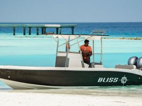 A speedboat named 'BUSS' is docked in shallow turquoise waters, with a crew member preparing for the next adventure. Ideal for exploring the beautiful coastline.