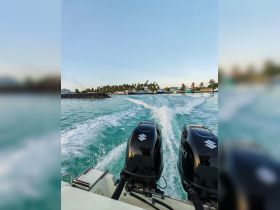 A dynamic view from the back of a speedboat cruising through turquoise waters, showcasing the powerful outboard engines and the scenic shoreline in the background.