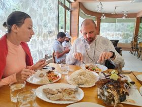 A couple enjoys a delicious seafood meal at a restaurant, featuring a variety of dishes including grilled fish and rice — perfect for food lovers seeking local cuisine.