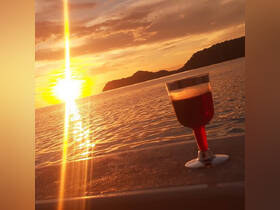 A beautiful sunset casts a golden glow over the water, with a cocktail glass in the foreground, perfect for romantic evenings on the boat.