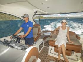 A man navigates the boat while a woman relaxes on the deck, enjoying the ocean breeze — a perfect scene for a day on the water.