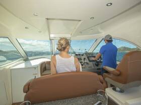 Inside view of a boat's helm area, featuring a couple at the controls, showcasing the spacious and modern interior design perfect for navigating the open waters.