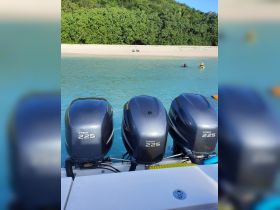 A scenic view featuring boat engines in the foreground with swimmers enjoying the clear waters near a sandy beach — a perfect spot for water activities.
