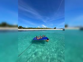 A lively group enjoys a day on a floating mat in crystal-clear waters, perfect for family fun and relaxation at the beach.