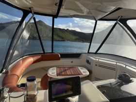 A cozy interior view of a boat's helm and seating area, showcasing the comfortable design and scenic waterfront backdrop.