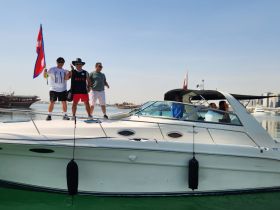 A lively group celebrates on the deck of a boat, proudly displaying a flag — perfect for memorable outings and adventures on the water.