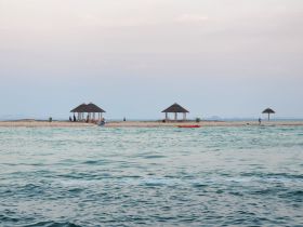 A picturesque view of a beach with huts and people enjoying kayaking, capturing the essence of a relaxing day by the water.
