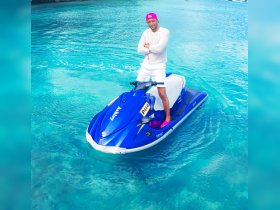 A man confidently poses on a vibrant blue jet ski, surrounded by stunning turquoise waters — a perfect snapshot of adventure on the water.