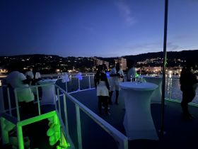 Guests enjoy a lively evening party on a boat, surrounded by stunning views and drinks, perfect for celebrations under the stars.