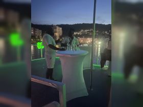 Two guests enjoy drinks on a boat during a vibrant evening, surrounded by a scenic waterfront view — perfect for nightlife and celebrations on the water.