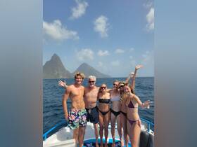 A cheerful group poses on a boat with stunning island scenery in the background, capturing a moment of joy and adventure on the water.