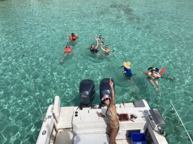 A lively group enjoys a fun day in the clear waters, celebrating with drinks and laughter while floating and swimming around the boat.