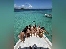 A lively group of friends enjoys a sunny day on the boat, celebrating and having fun in the clear turquoise waters near an island — perfect for unforgettable summer adventures.