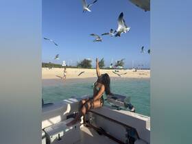 A woman enjoys the sun on a boat while seagulls fly around, capturing the essence of a fun beach day. Perfect for showcasing lively moments on the water.