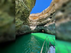A stunning view of a boat navigating through a scenic cave with vibrant green waters, showcasing the beauty of nature and adventure on the water.