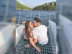 A couple shares a romantic kiss on the deck of a boat, surrounded by stunning coastal scenery — perfect for memorable moments on the water.