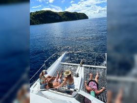 A group of friends relaxes on the netting of a catamaran, enjoying the sun and ocean views — a perfect day on the water.