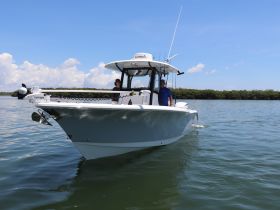A sleek boat navigates through calm waters with two individuals onboard, showcasing a perfect day for boating adventures.
