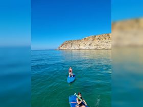 Two young girls paddleboard in calm waters near a stunning coastline, showcasing a perfect day of adventure and fun on the water.