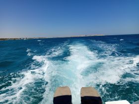 A scenic view from the back of a boat, showcasing the wake and vibrant blue waters as it moves along the coastline, perfect for capturing the essence of a day on the water.