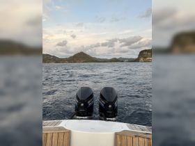 A view from the back of a boat showcasing twin outboard motors against a backdrop of lush hills and a serene sea, perfect for exploring coastal destinations.