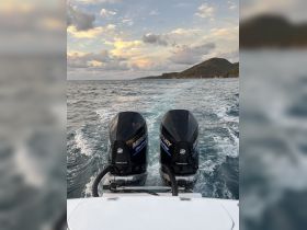 A view of twin Mercury outboard motors on a boat, cutting through the water with a scenic backdrop of clouds and hills — perfect for showcasing the power and performance of the vessel.