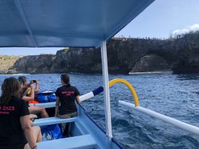 A group of friends enjoys a boat tour in Bali, capturing the stunning coastline and natural arch in the background — a perfect adventure for exploring the island's beauty.