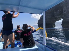 A group of friends aboard a boat in Bali, enjoying the stunning ocean scenery and exploring natural rock formations — a perfect adventure on the water.
