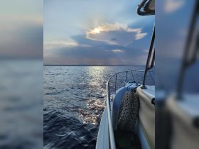 A serene view of a boat's side against a backdrop of shimmering water and a dramatic sky, perfect for showcasing the beauty of a day on the water.