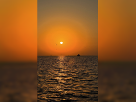 A serene sunset over the water with a silhouette of a boat in the distance, creating a picturesque scene perfect for evening cruises.