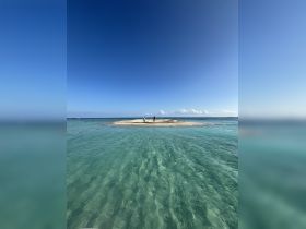 Two individuals explore a picturesque sandbar surrounded by crystal-clear waters, perfect for island hopping adventures and beach relaxation.