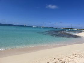 A stunning view of a tranquil beach with turquoise waters and sailboats in the distance, perfect for a relaxing day by the shore.