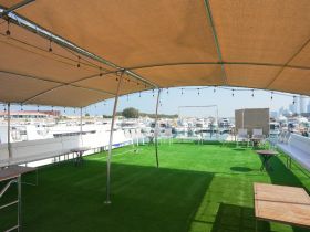 A spacious lounge area on a boat featuring comfortable seating and shade, perfect for relaxing while enjoying views of the marina.