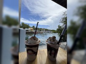 Two delicious cocktails topped with whipped cream are served at a waterfront bar, perfect for enjoying the scenic marina views.