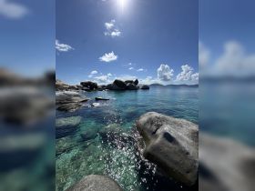 A stunning view of crystal-clear waters and rocky formations under a bright sun, perfect for showcasing the natural beauty of island destinations.